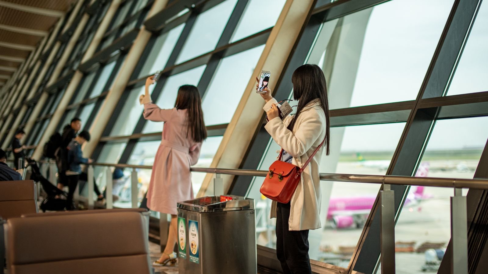 Travellers watching aircraft from a terminal window.
